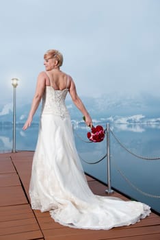An elderly bride in a long wedding dress with veil holds her bridal bouquet