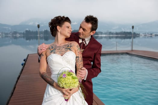 A young bride with many tattoos stands with her husband at the lido near Lake Wolfgang