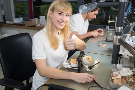 Dental technicial in a dental laboratory with articulator showing thumbs up