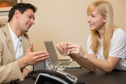 Dental technicial showing a model of a dental prosthesis to a customer or patient in her office