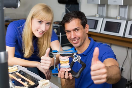 Two dental technicians with articulator in a dental lab showing thumbs up