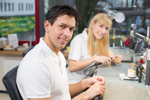 Dental technician in a lab polishing gold tooth and smiling into the camera