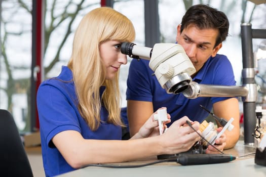 Dental technicians working on mold under a microscope in a lab