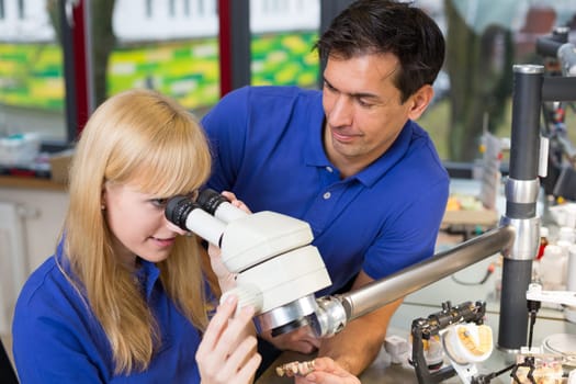 apprentice and dental technician look at prosthesis under a microscope in a lab