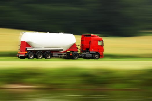 large white cistern truck speeding on highway with blurred countryside panorama in background