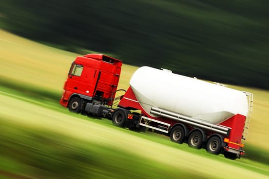 large white cistern truck speeding on highway with blurred countryside panorama in background