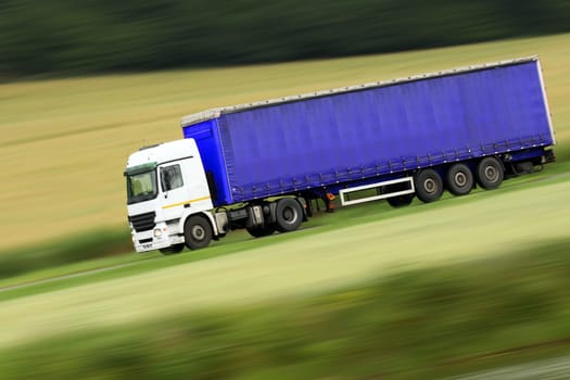 large blue truck speeding on highway with blurred countryside panorama in background