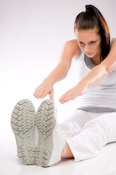 Young Caucasian woman stretching towards her feet on white background