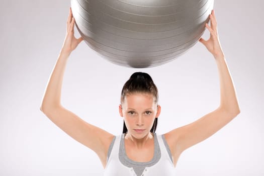 Portrait of young woman exercising with fitness ball held above