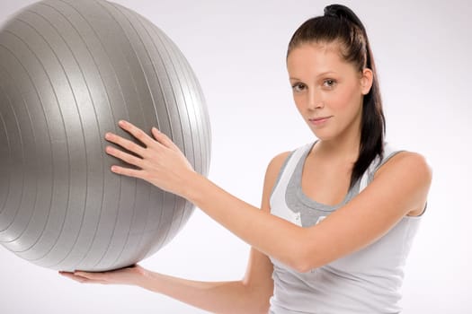 Young Caucasian brunette woman holding fitness ball on white background