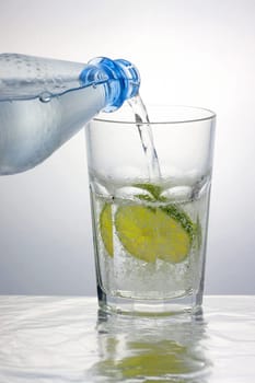 Pouring sparkling water into a caipirinha glass with a lemon slice