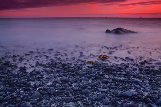 Pebble beach with red skies by sunset on Lofoten islands in Norway