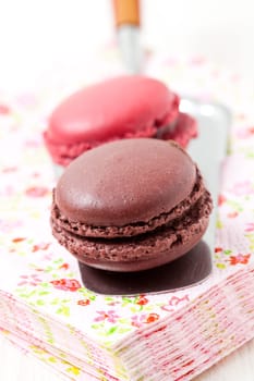 Close-up of two colorful macaroons on serviette and cake server on light background