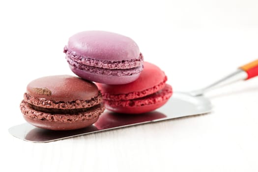 Close-up of three colorful macaroons on cake server on light background