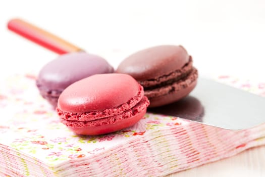 Close-up of three colorful macaroons on serviette and cake server on light background