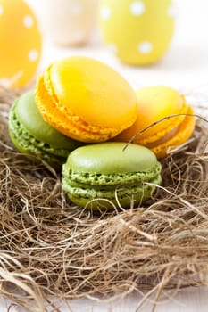 Close-up of colorful macaroons resting in straw nest and Easter eggs on light background