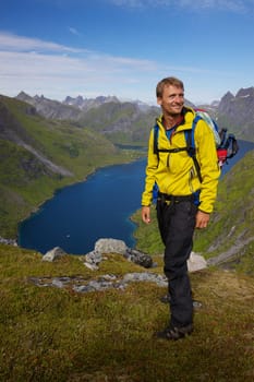 Young active man with backpack hiking on Lofoten islands in Norway on sunny day