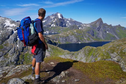 Young active man with backpack hiking on Lofoten islands in Norway on sunny day