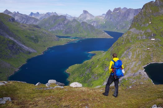 Young active man with backpack hiking on Lofoten islands in Norway on sunny day with scenic panorama in the background