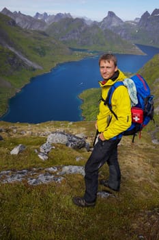 Young active man with backpack hiking on Lofoten islands in Norway on sunny day
