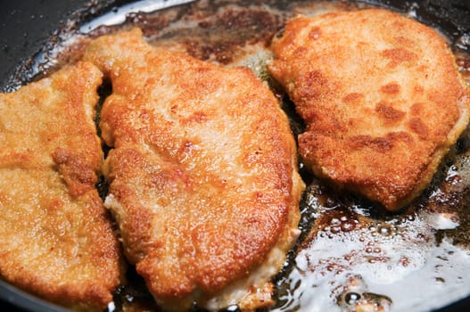 Close-up of a frying pan with two golden yellow schnitzel meat slices frying in it