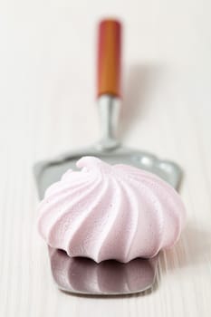 Closeup of pink meringue resting on server utensil against light background