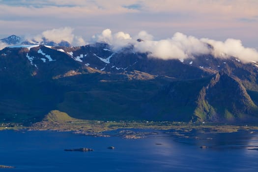 Scenic mountain peaks on Lofoten islands in Norway covered with clouds with small fishing villages on the coast