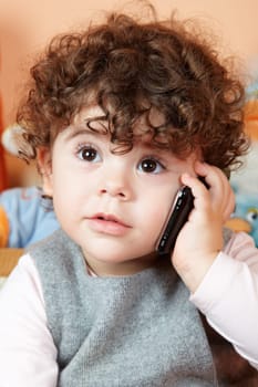 Two year old girl with curly hair talking on phone.