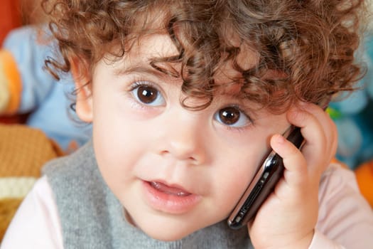 Two year old girl with curly hair talking on phone.