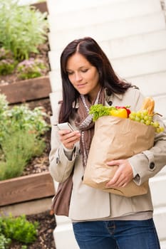 Young woman holding bag groceries vegetables shopping smart phone texting