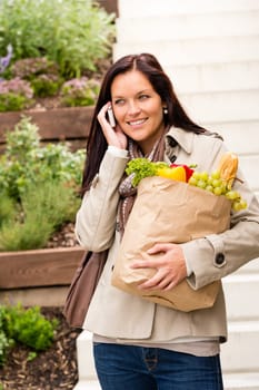 Happy woman shopping vegetables calling cell phone paper bag