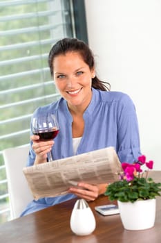 Cheerful woman reading drinking wine newspaper living room