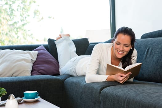 Young woman lying reading book couch sofa living room