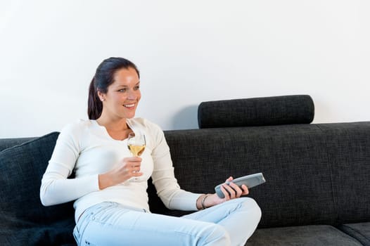 Happy woman lying down couch watching TV drinking wine