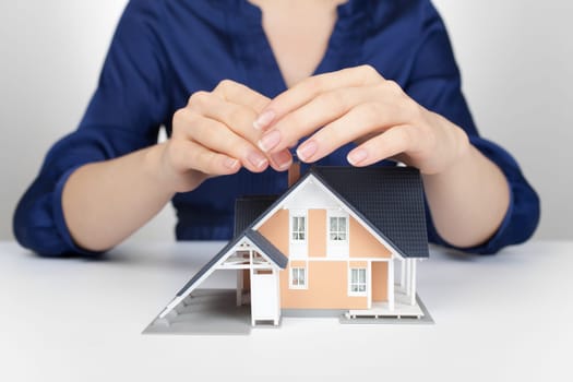 Property insurance concept - woman protect model of the house.