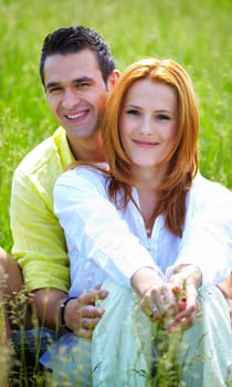 Young couple in their 20s holding eachother outdoor in a grass field.