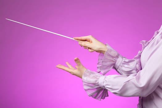 Female orchestra conductor hands, one with baton. Pink background.