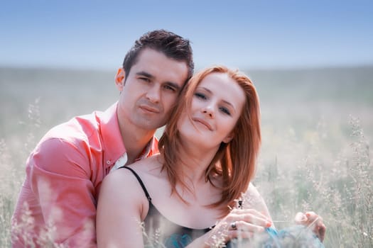 Young couple in their 20s holding eachother outdoor in a grass field.