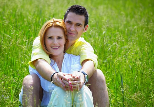 Young couple in their 20s holding eachother outdoor in a grass field.