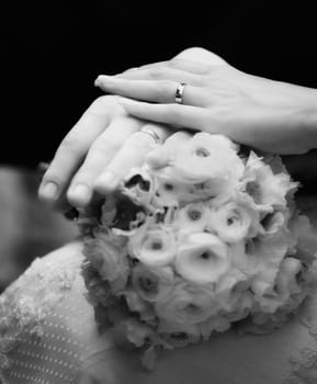 Closeup of hands of newly weds and flower bouquet in black and white, soft focus.