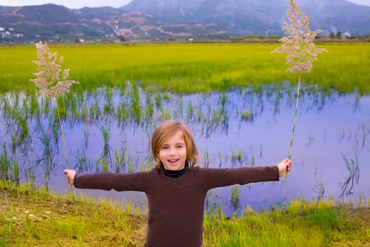 Blond kid girl outdoor holding spike in wetlands lake meadow