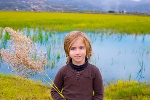 Blond kid girl outdoor holding spike in wetlands lake meadow