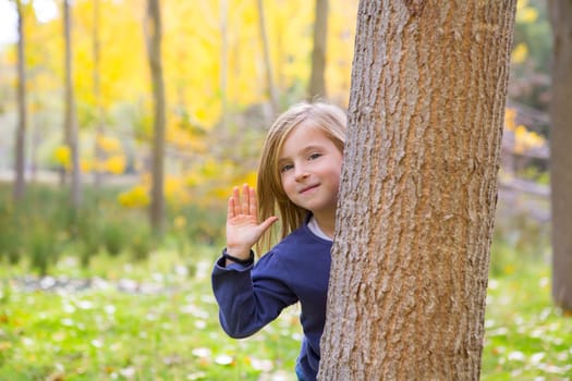 Autumn forest with child girl greeting hand behind poplar tree trunk