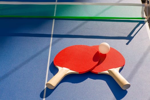 table tennis ping pong two paddles and white ball on blue board