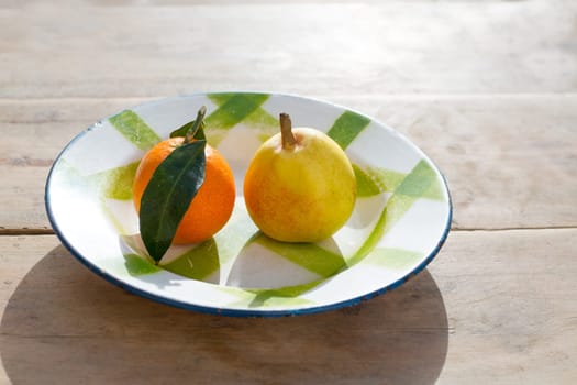 fruits tangerine and pear in vintage porcelain dish plate on retro wood table