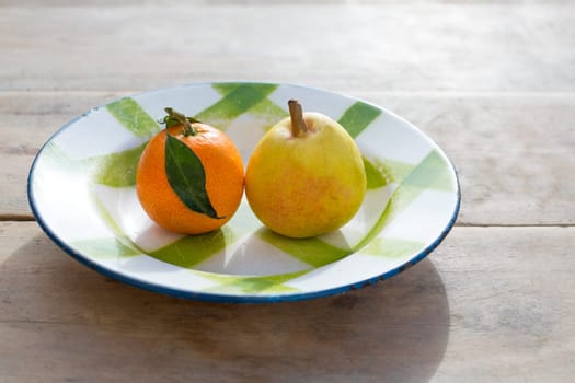 fruits tangerine and pear in vintage porcelain dish plate on retro wood table