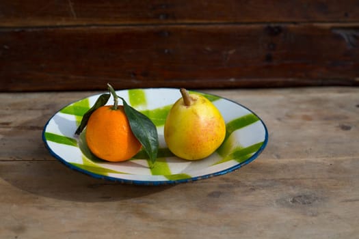 fruits tangerine and pear in vintage porcelain dish plate on retro wood table