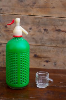 ancient soda bottle with little cup in wooden background