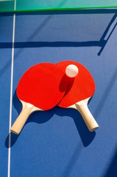 table tennis ping pong two paddles and white ball on blue board