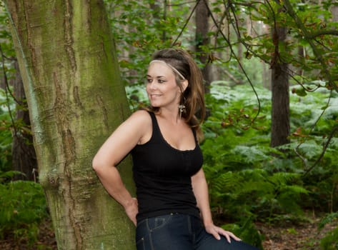 attractive woman in woodland setting leaning against a tree